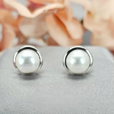A pair of classic freshwater pearl stud earrings made of sterling silver, displayed against a floral background.