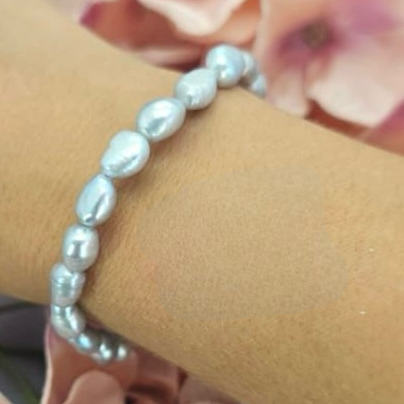 A grey freshwater pearl bracelet on a person's wrist, with flowers in the background.