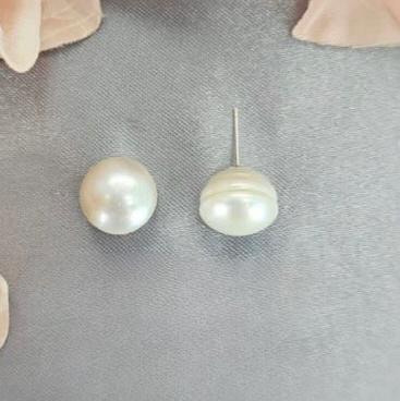 A pair of white freshwater pearl stud earrings on a textured background with floral accents.