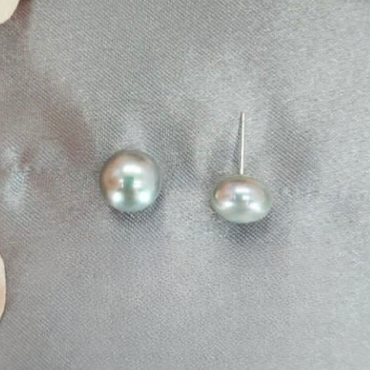 A close-up image of a pair of sterling silver freshwater pearl stud earrings on a textured grey background.