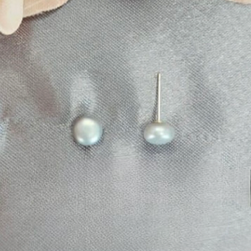 A close-up image of a pair of grey freshwater pearl stud earrings on a textured grey background.