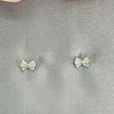 A pair of sterling silver bow-shaped earrings with cubic zirconia details, displayed against a grey background with a pink floral pattern.