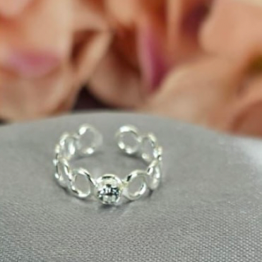 A silver toe ring with a cubic zirconia center, displayed on a grey surface with floral background.