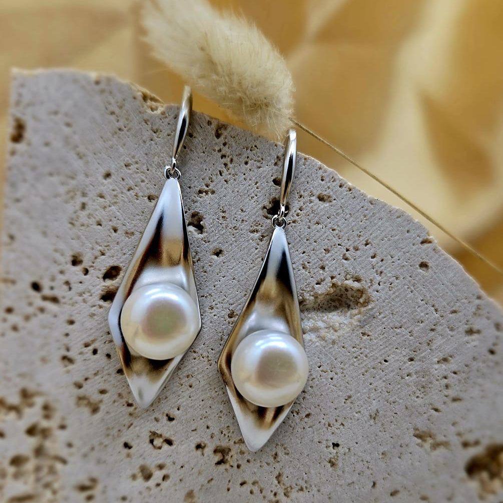 Pearl earrings on a textured stone surface with a blurred yellow background