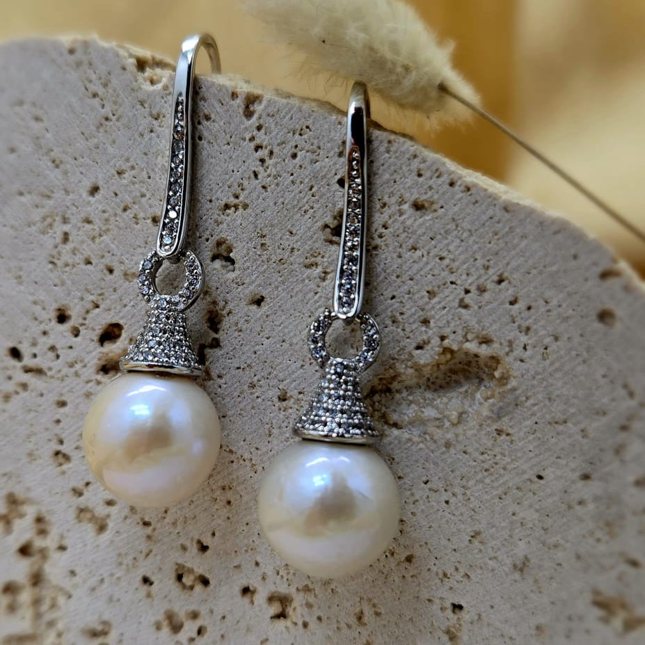 Pearl earrings with silver hooks on a textured surface with a blurred natural background