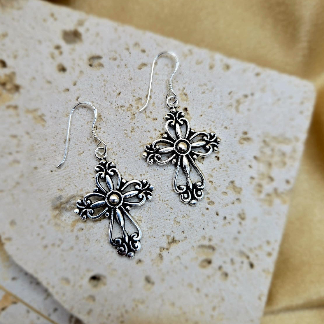 Silver cross earrings on a textured stone surface