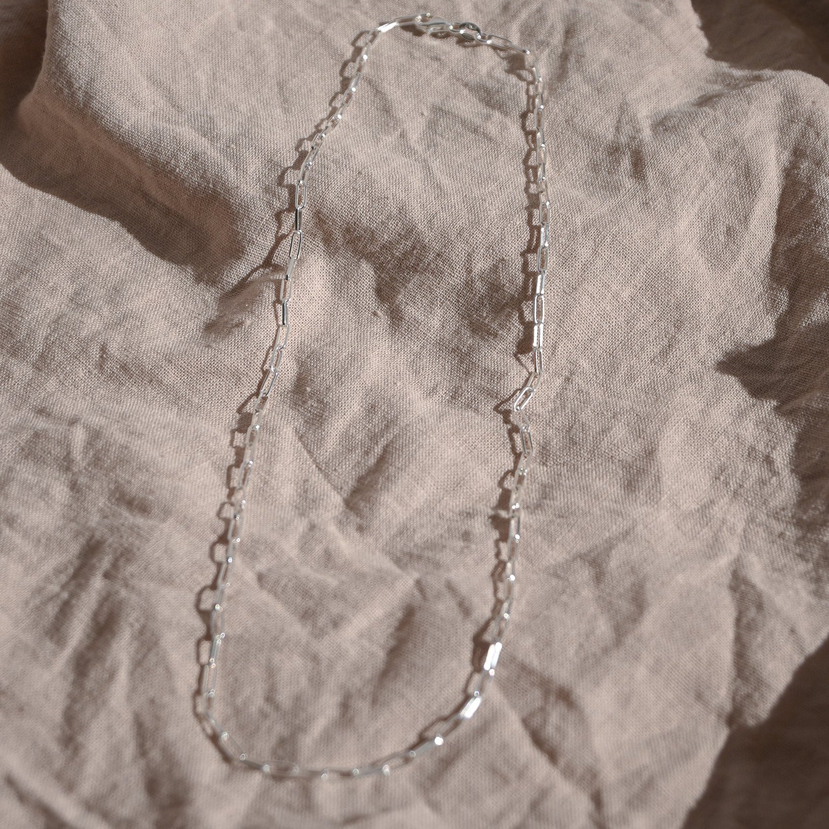 Silver chain necklace on a textured beige surface