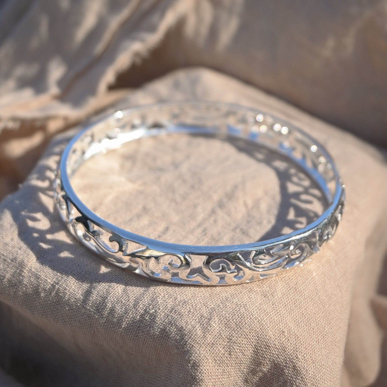 Silver bracelet with intricate design on a beige fabric background