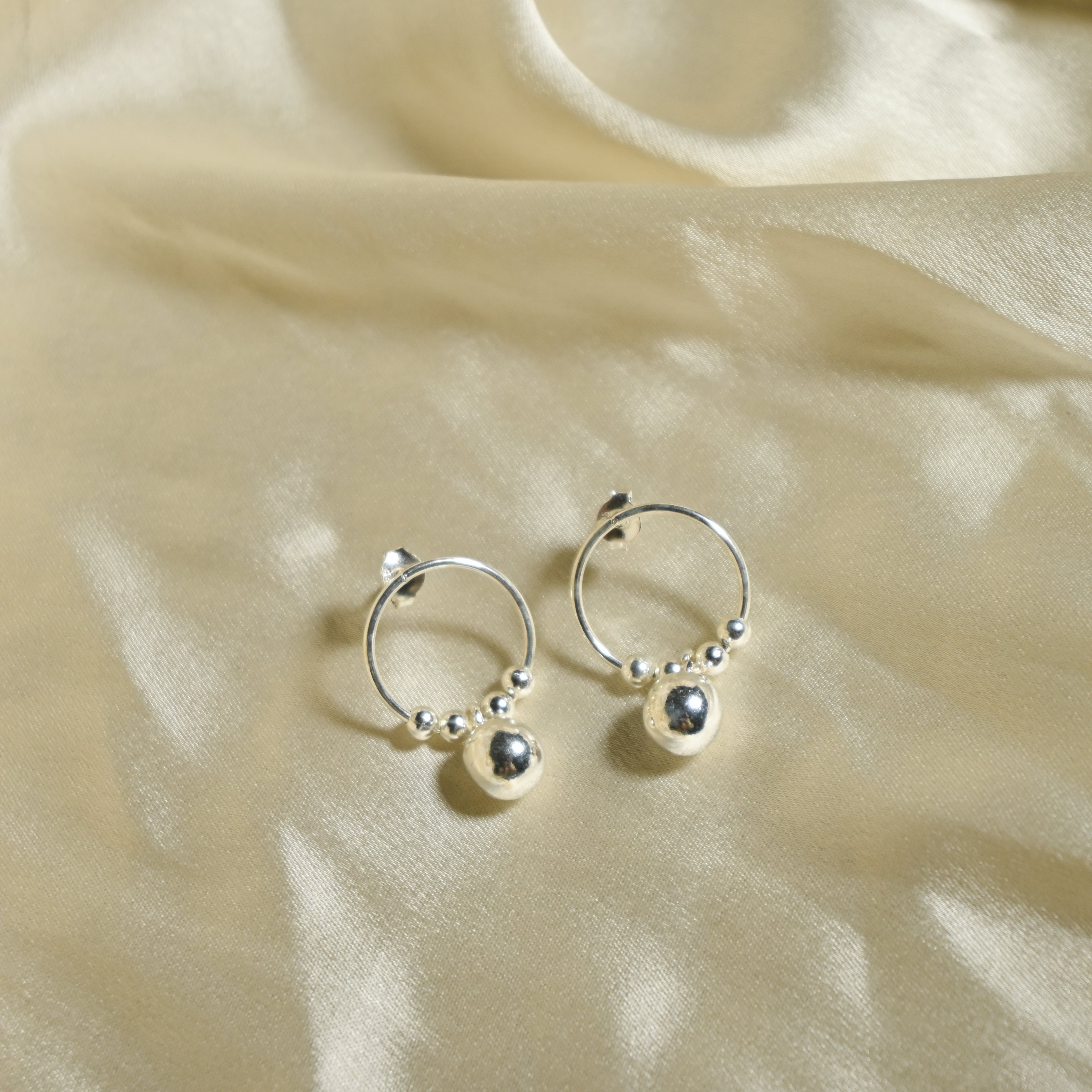 Silver hoop earrings with small spherical charms on a beige fabric background