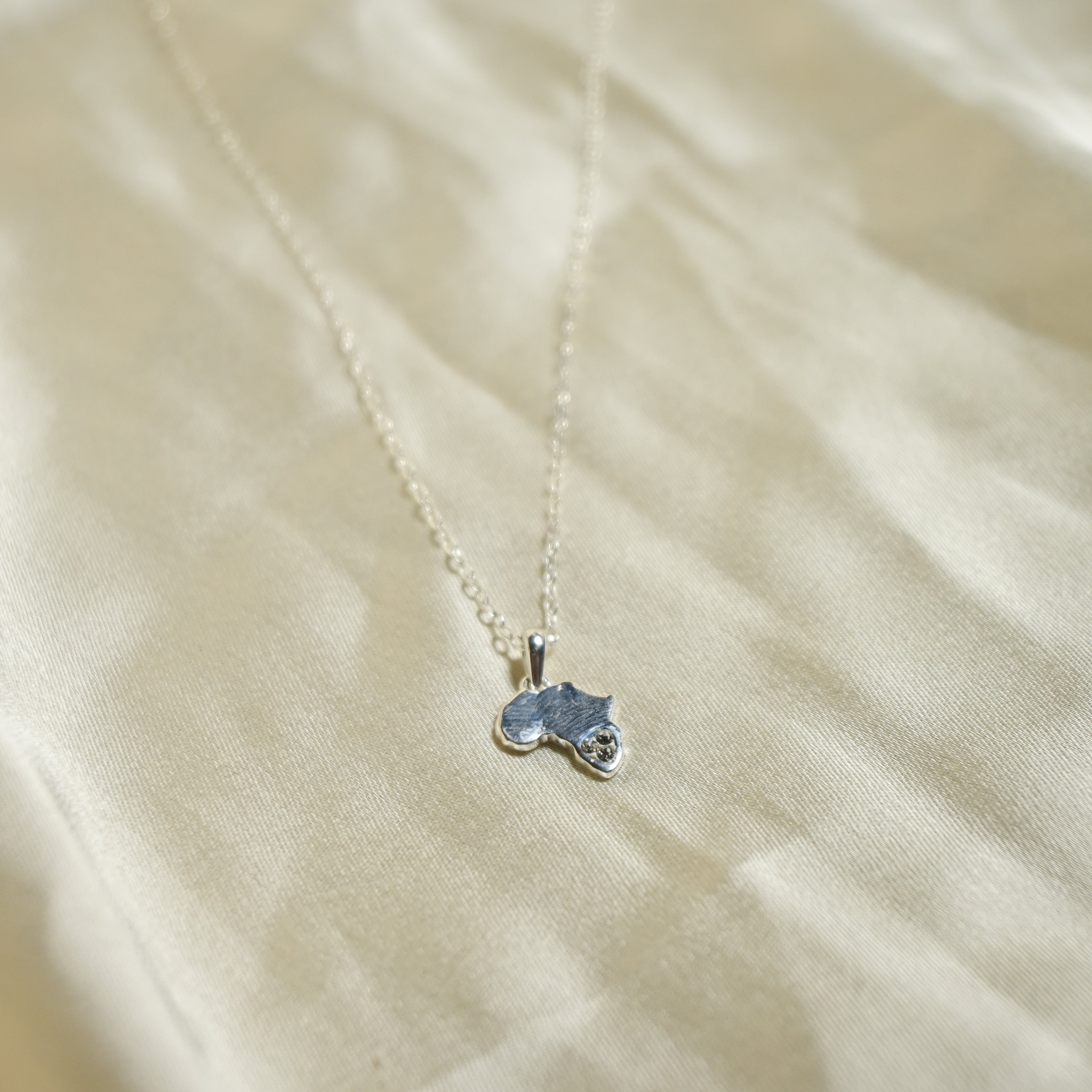 Small blue pendant on a chain against a beige fabric background