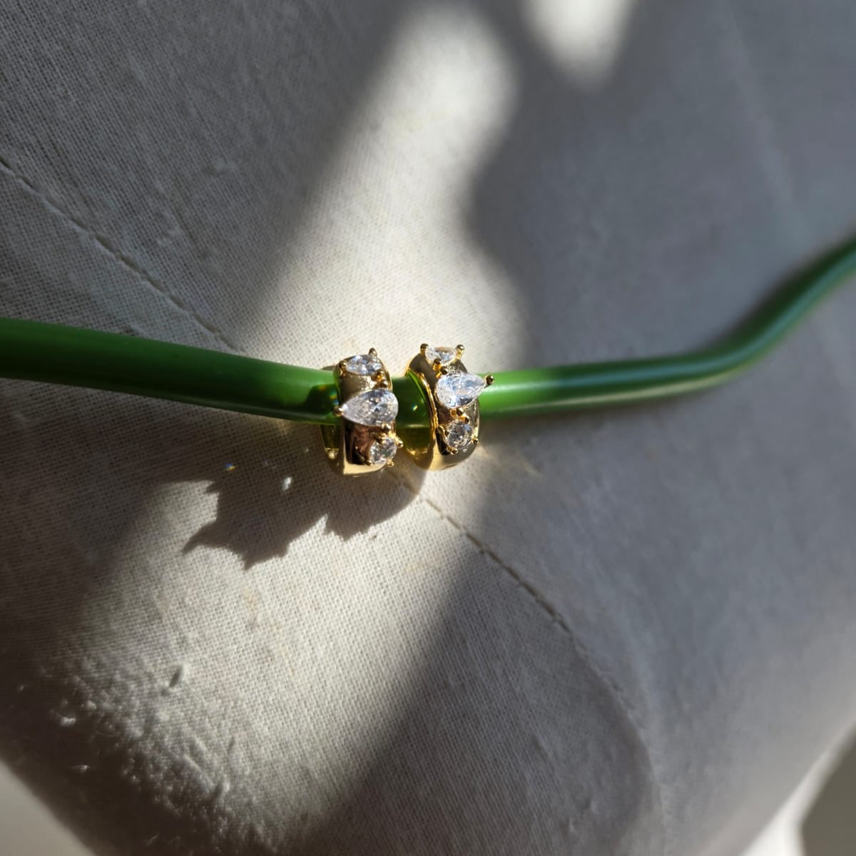 Gold earring with clear stones on a green stem against a light gray background