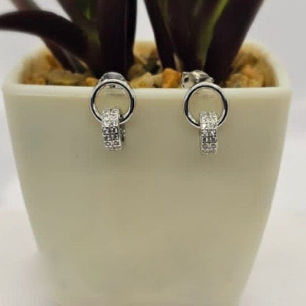 A pair of sterling silver double ring studs with cubic zirconia detail, displayed against a white pot with a plant.