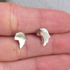 Silver earrings held between two fingers on a neutral background