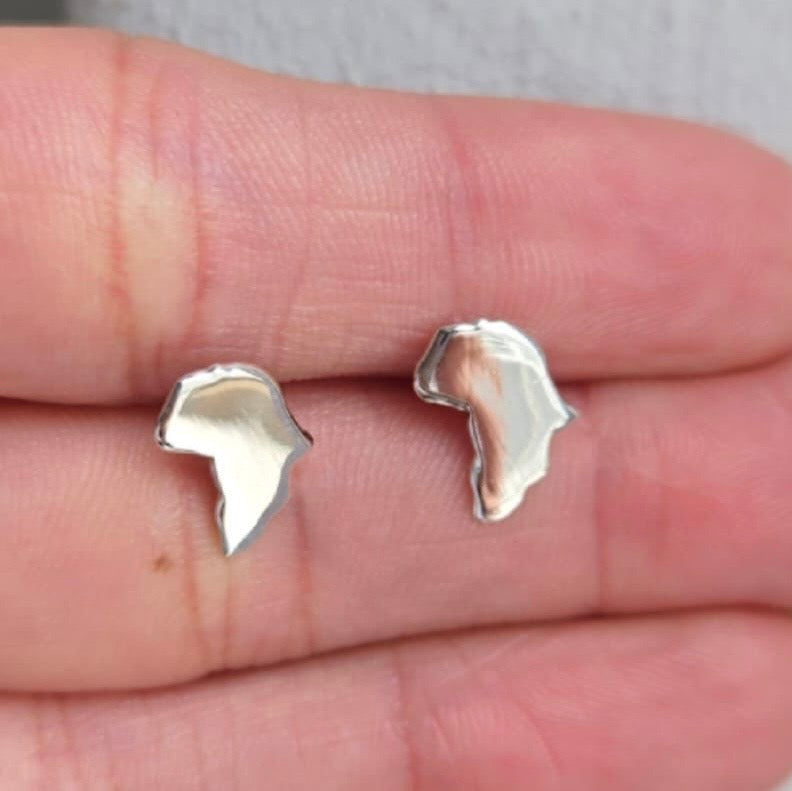 Silver earrings held between two fingers on a neutral background