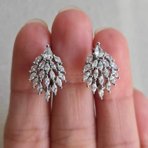 Silver leaf-shaped earrings held between fingers against a neutral background
