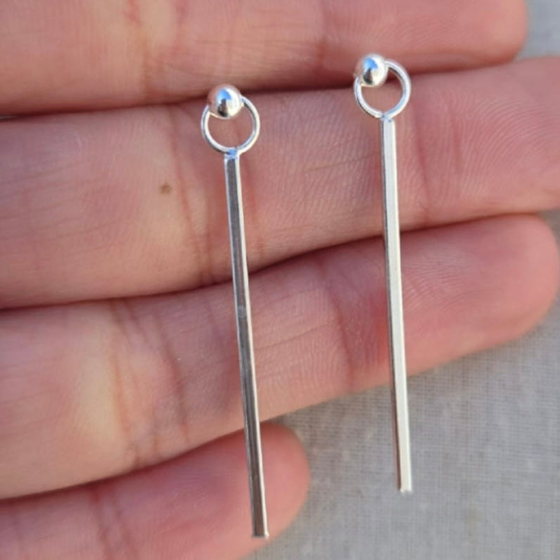 Silver earrings held between fingers on a neutral background