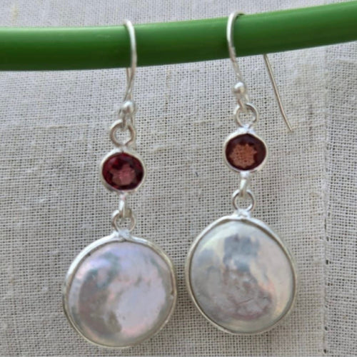 Pair of silver earrings with round stones on a green stick against a textured fabric background