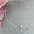 A sterling silver interlinked circle bracelet displayed on a surface with a background of flower petals.