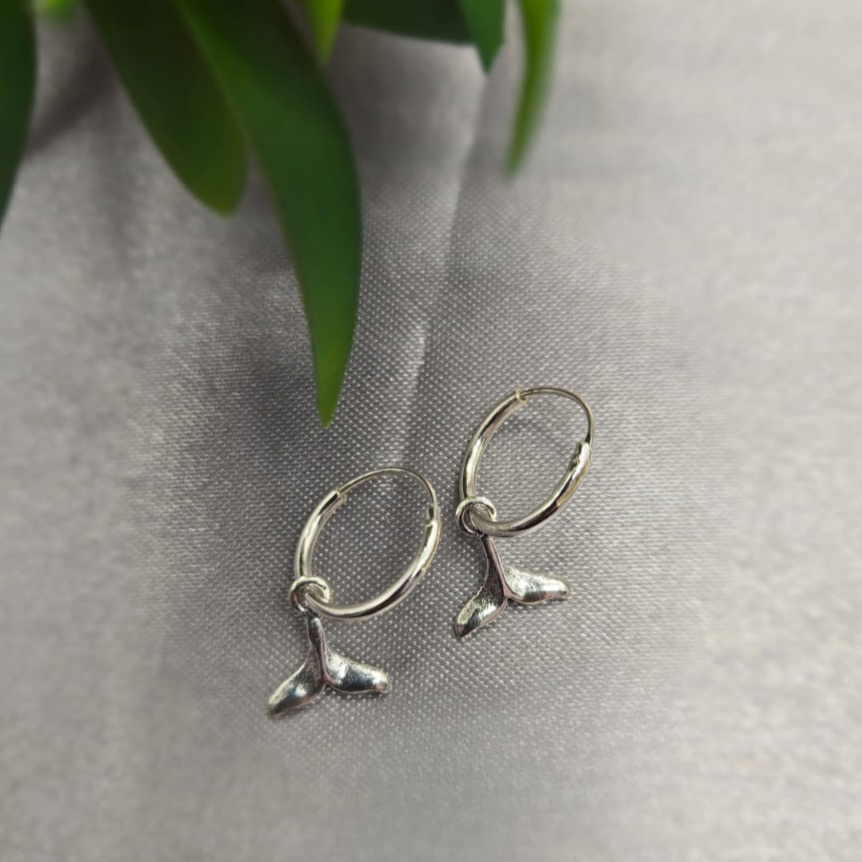 Silver earrings on a gray surface with a plant in the background