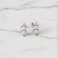 Pair of pearl earrings on a light gray surface with a pink fabric background