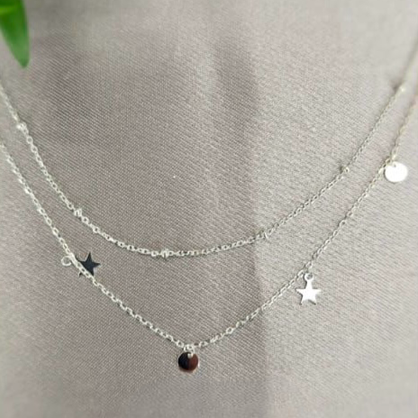 A sterling silver double necklace with a moon and star design, displayed on a textured background.