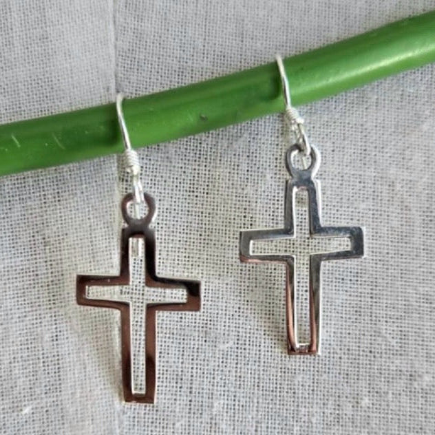 Silver cross-shaped earrings hanging from a green stick on a textured fabric background