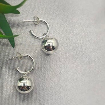A pair of sterling silver hoop earrings with a 14mm ball charm, displayed on a white fabric surface.