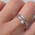Silver ring with a pearl on a finger against a neutral background