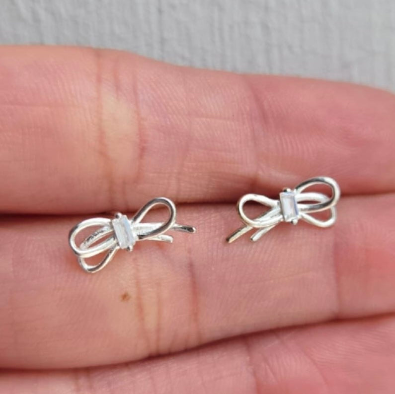 Silver bow-shaped earrings on a hand