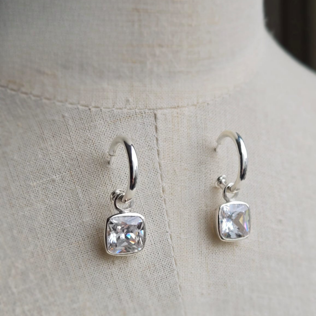 Silver hoop earrings with square gemstones on a light fabric background