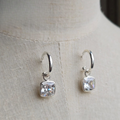 Silver hoop earrings with square gemstones on a light fabric background