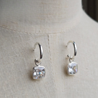 Silver hoop earrings with square gemstones on a light fabric background