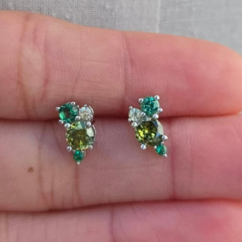 Pair of green gemstone earrings held between fingers against a neutral background
