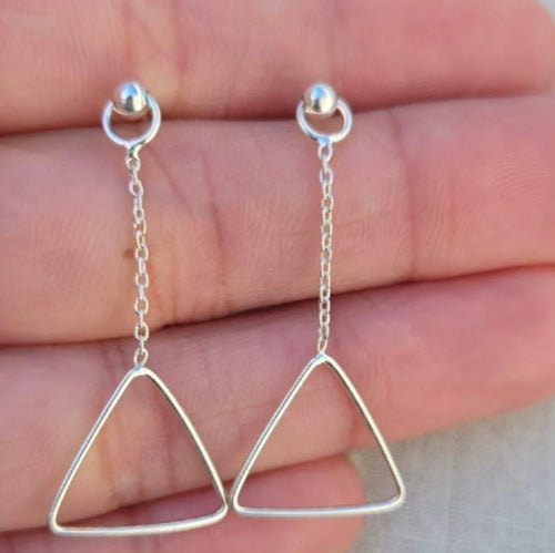 Silver triangle earrings held between fingers against a neutral background