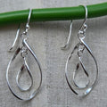 Silver teardrop earrings hanging on a green rod against a gray background