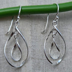 Silver teardrop earrings hanging on a green rod against a gray background