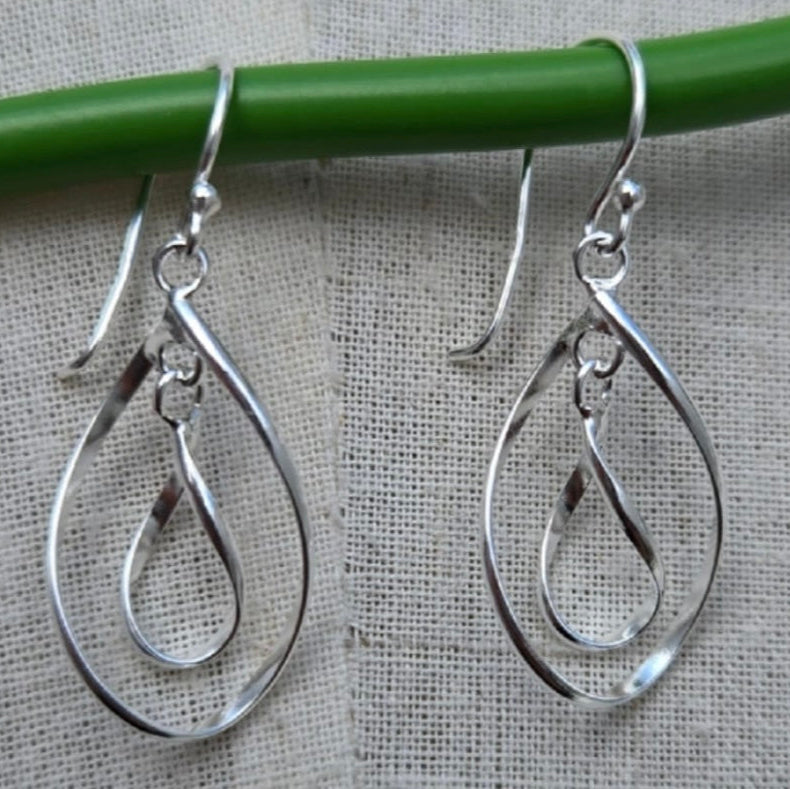 Silver teardrop earrings hanging on a green rod against a gray background