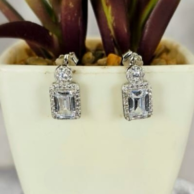A pair of rectangular cubic zirconia stud earrings placed in a white vase with a green plant.
