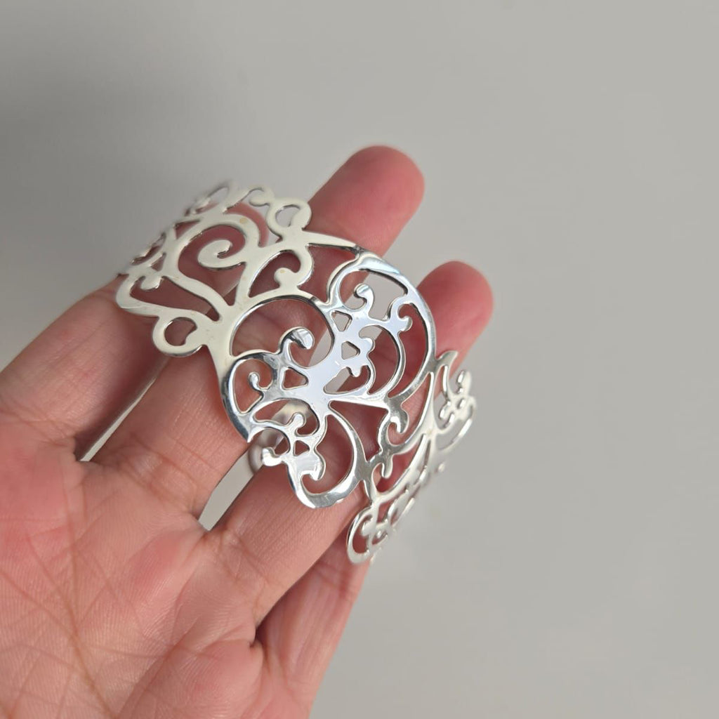 Silver decorative hair clip held in a hand against a neutral background