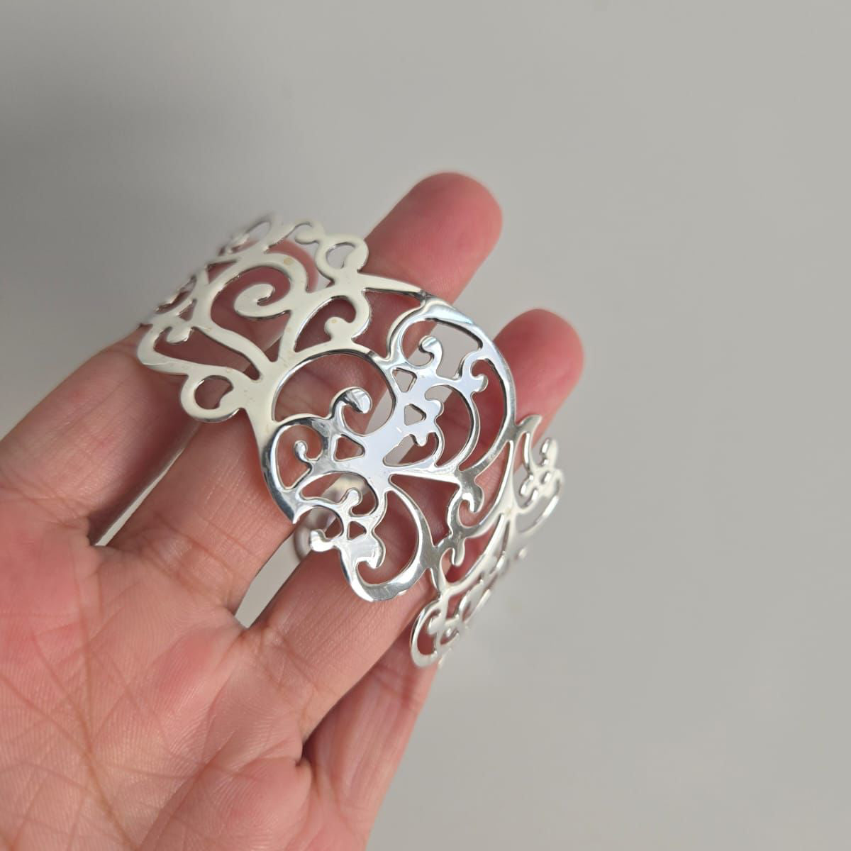 Silver decorative hair clip held in a hand against a neutral background
