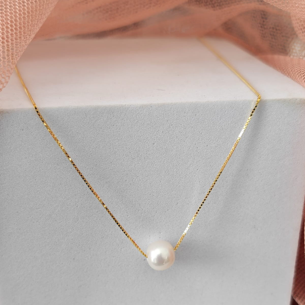 Pearl necklace on a gray jewelry box with pink fabric in the background