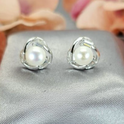 A pair of sterling silver bling flower earrings with freshwater pearl embellishments, displayed on a grey fabric surface with a floral background.