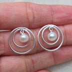 Silver hoop earrings with pearls held in a hand on a neutral background