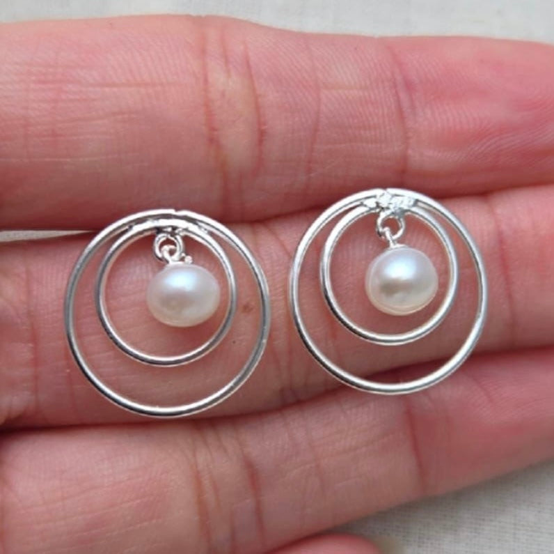Silver hoop earrings with pearls held in a hand on a neutral background