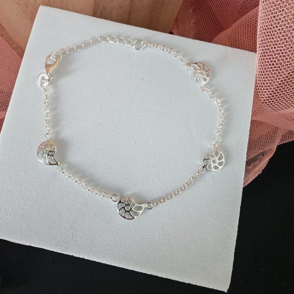 Silver bracelet with heart charms on a white card with a pink fabric background