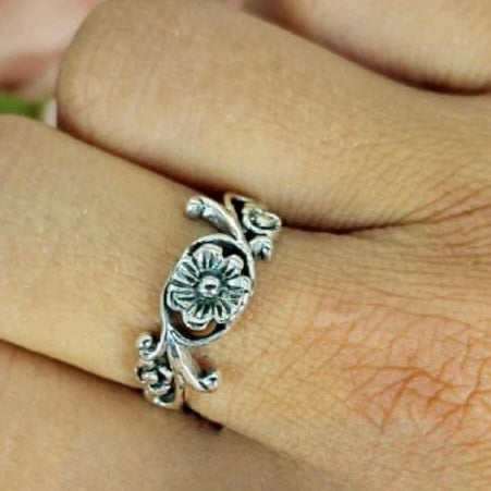 A sterling silver ring with a floral design worn on a person's finger.