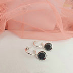 Silver hoop earrings with black stones on a white surface with pink fabric in the background