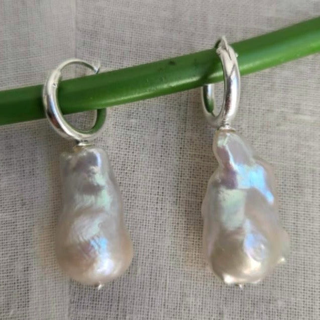 Pearl earrings hanging from a green stick on a textured fabric background