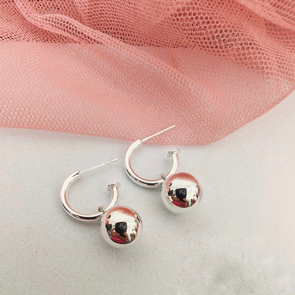 Silver hoop earrings with round balls on a pink fabric background
