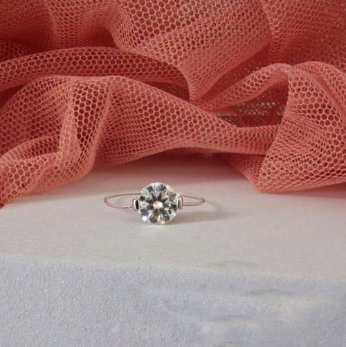 Silver ring with a diamond on a pink fabric background